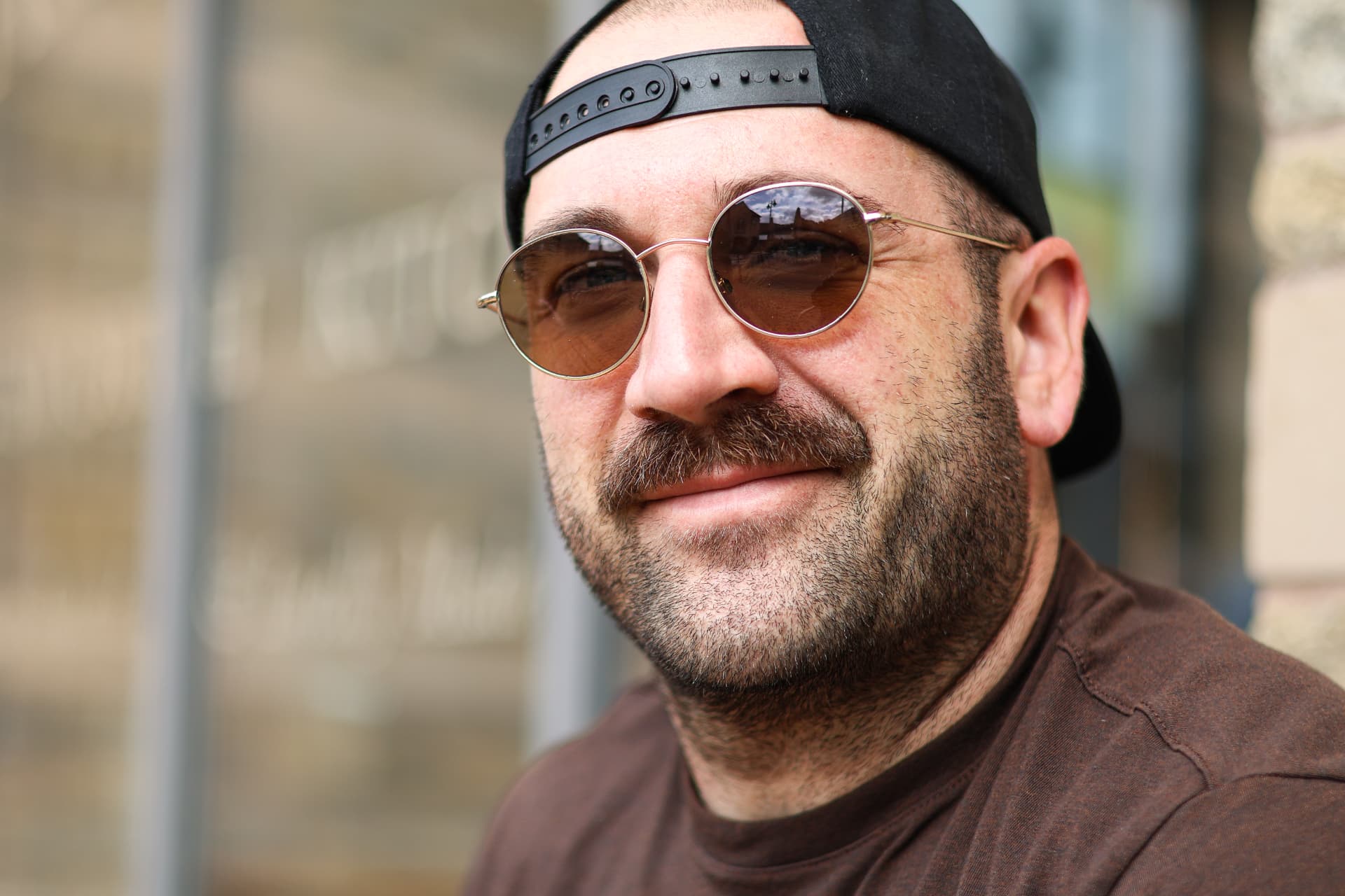 Close portrait of a man wearing round sunglasses and a backwards cap